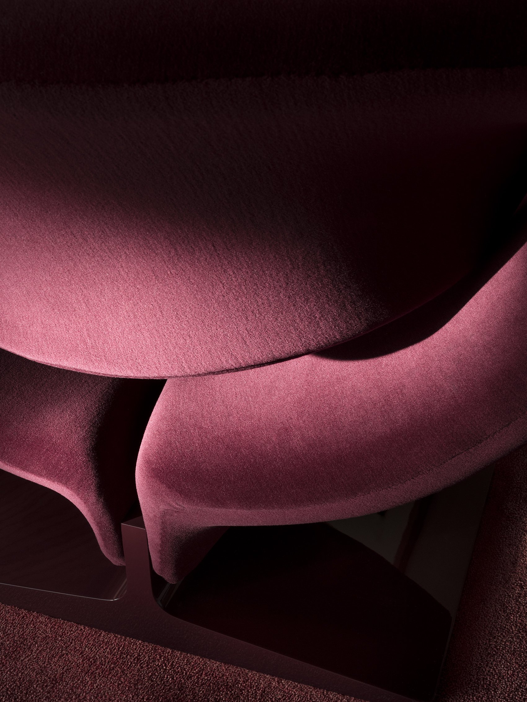 Close-up of Ribbon's burgundy upholstered curve, folded seat and shadowed opening